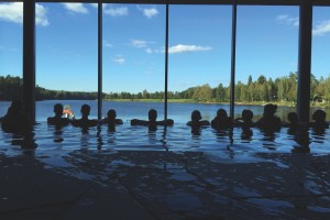 Gäster i inomhuspool med panoramautsikt över sjö och skog på svenskt spahotell