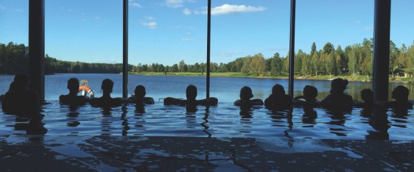 Gäster i inomhuspool med panoramautsikt över sjö och skog på svenskt spahotell