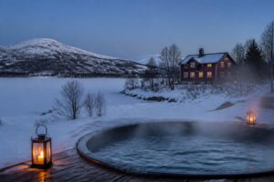 Stämningsbild: snöiga fjäll i blå timmen med en ångande utomhuspool och en röd stuga – genererad bild, inte ett foto från något av hotellen